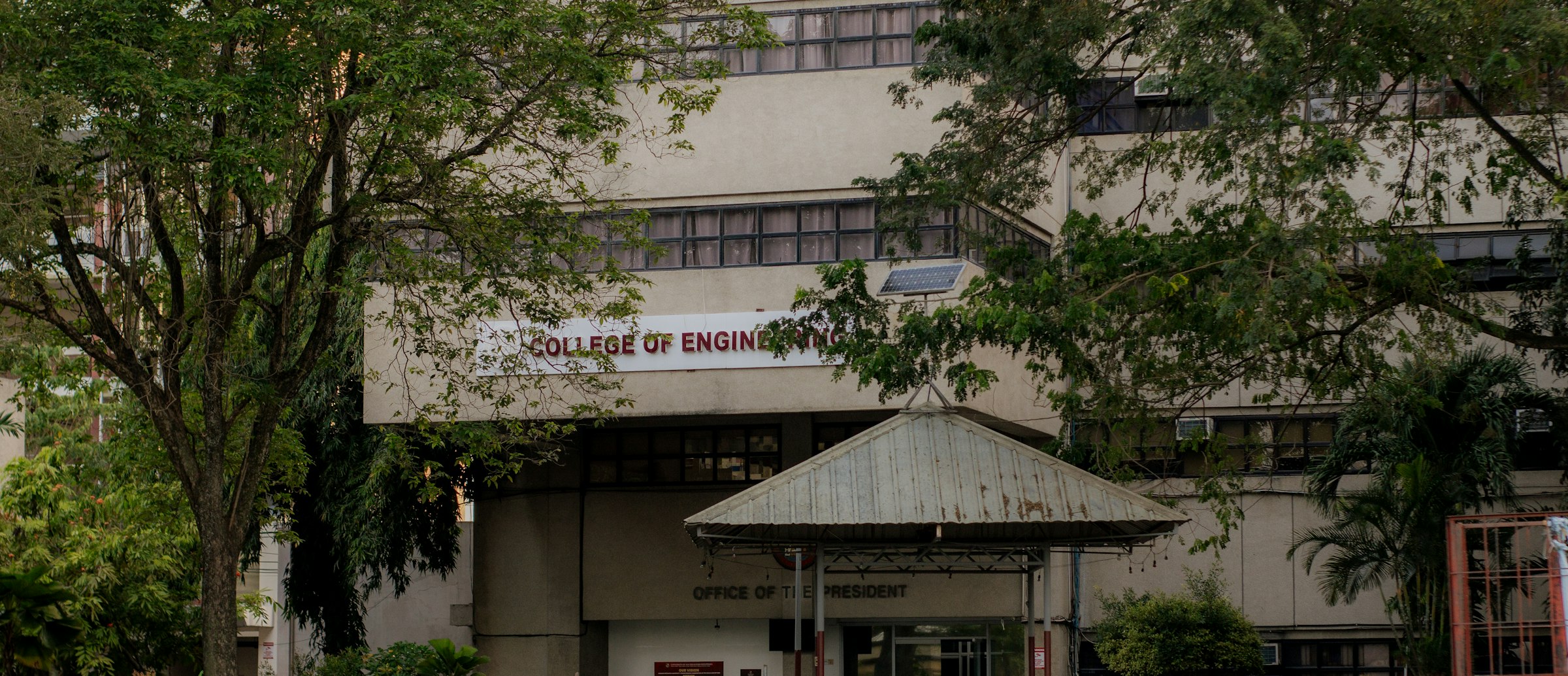 A college building is seen behind some trees.