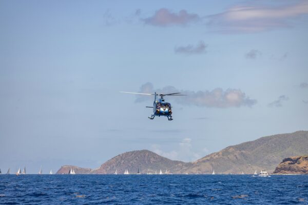 A helicopter flies over the ocean and mountains.