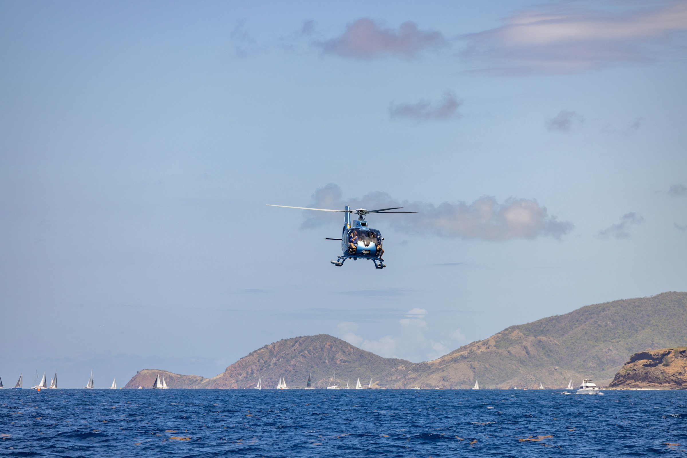 A helicopter flies over the ocean and mountains.
