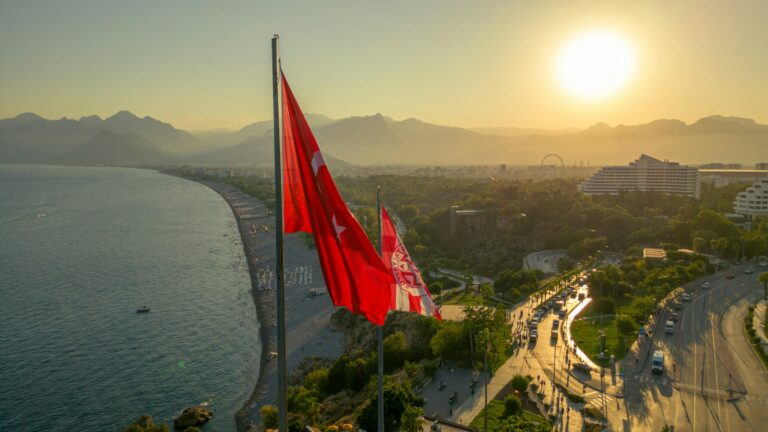 Turkish flag flies over a coastal city at sunset.