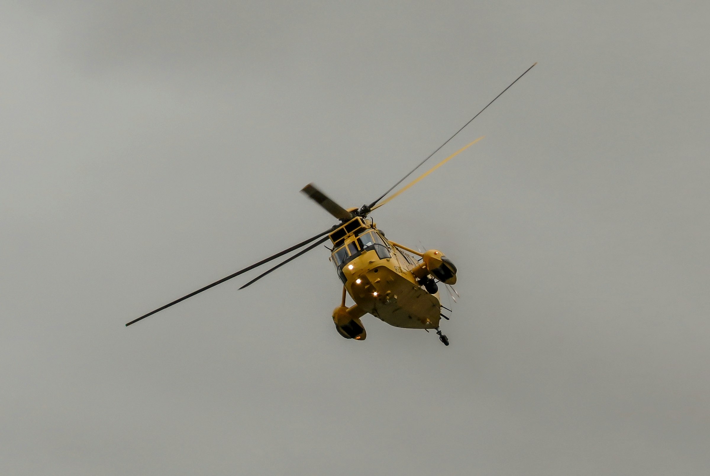 a yellow helicopter flying through a cloudy sky
