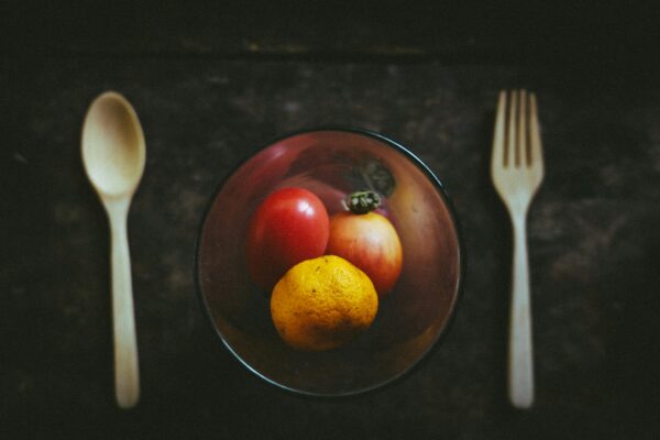 amber glass bowl with fruits besides white spoon and fork