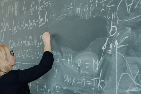 Woman writing complex mathematical equations on a chalkboard.