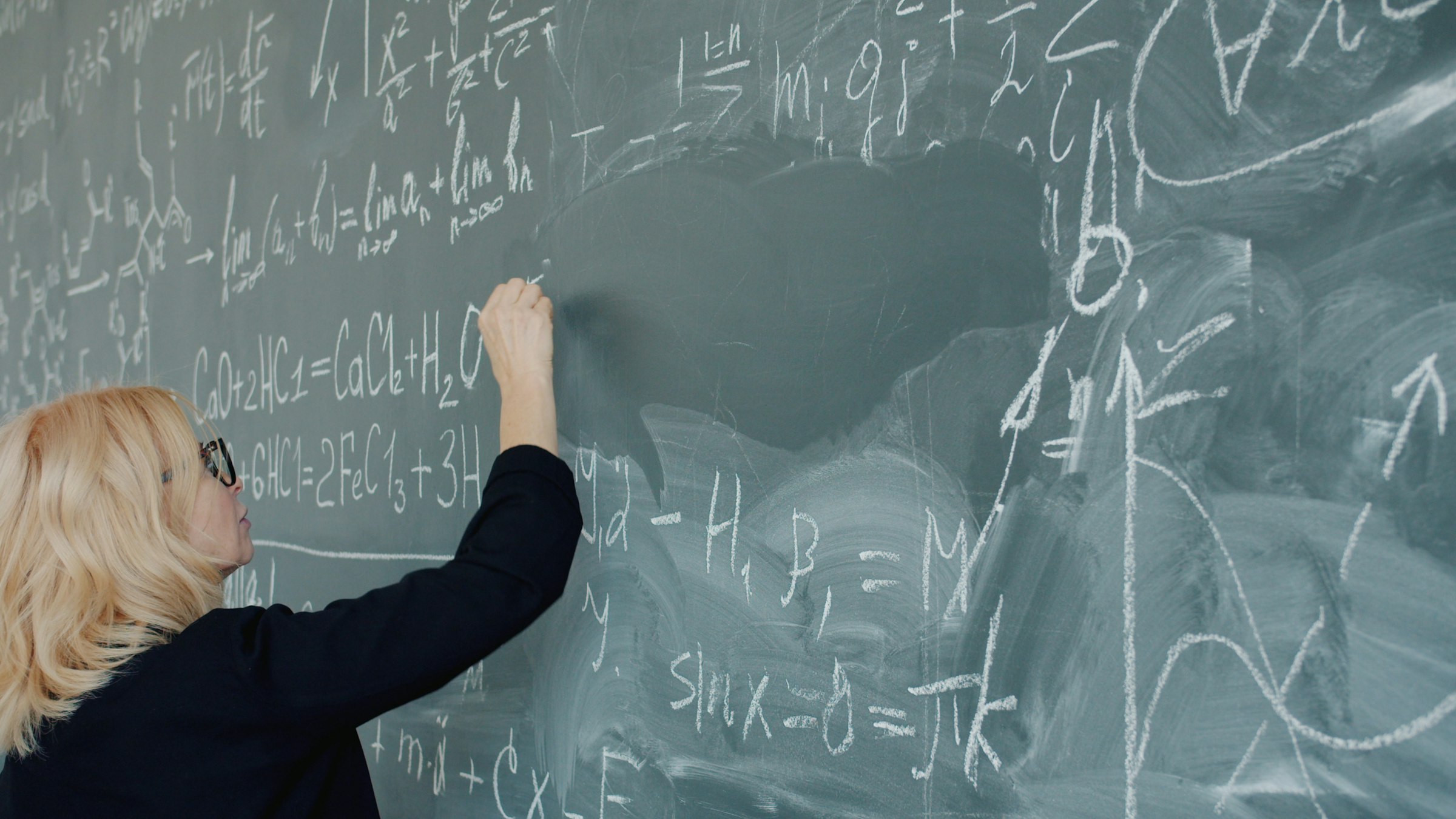 Woman writing complex mathematical equations on a chalkboard.