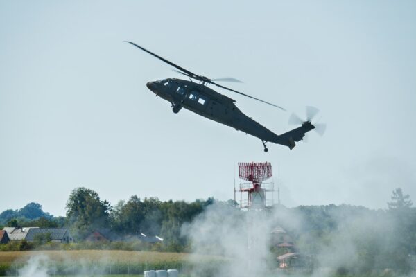 A dark helicopter ascends with smoke below.