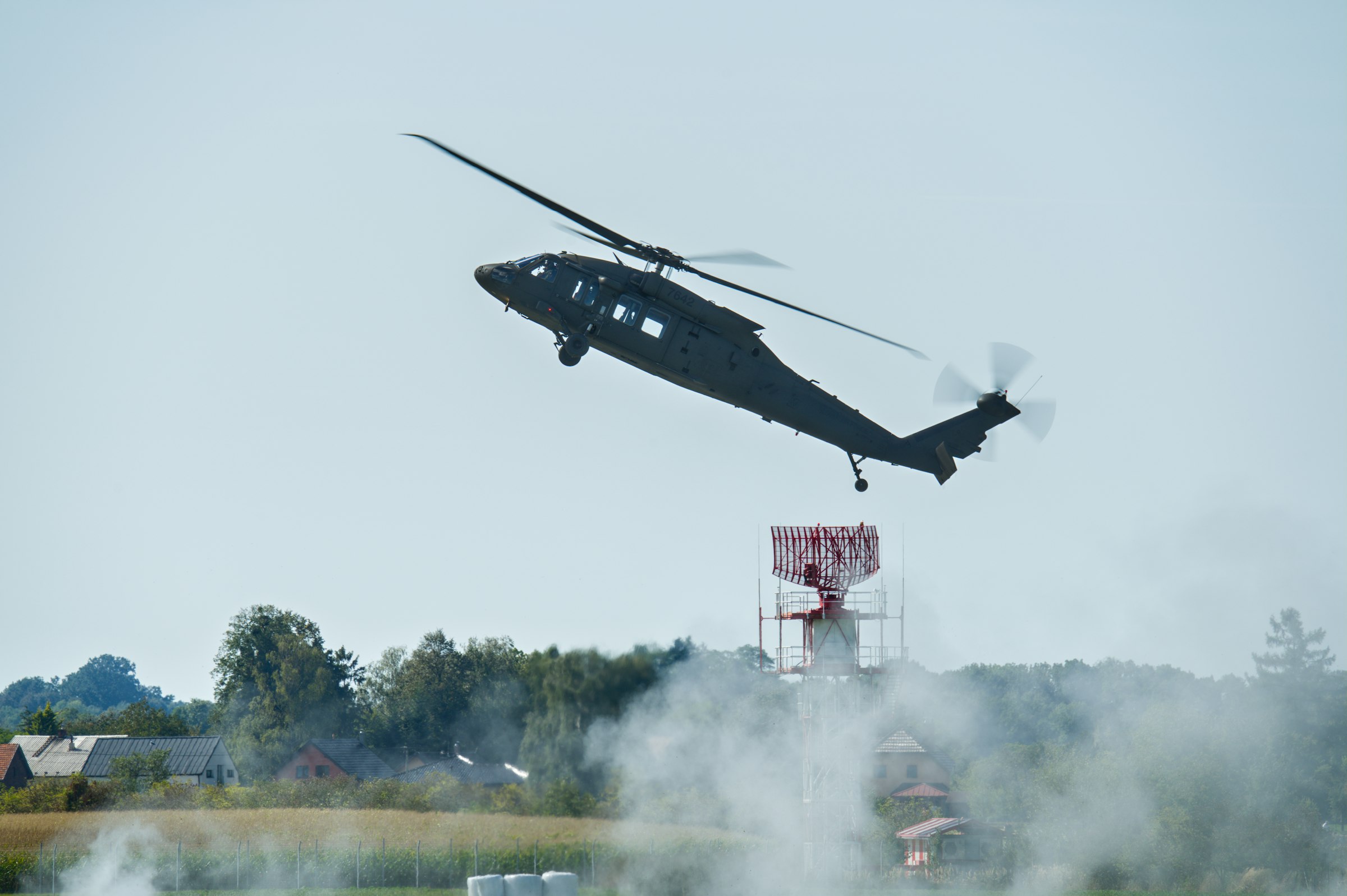 A dark helicopter ascends with smoke below.