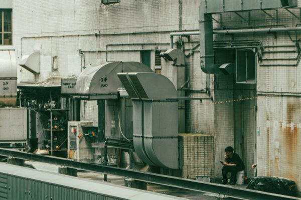 A person sits amidst industrial machinery outdoors.