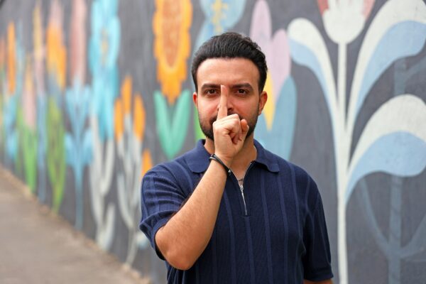 Man touches nose in front of colorful mural