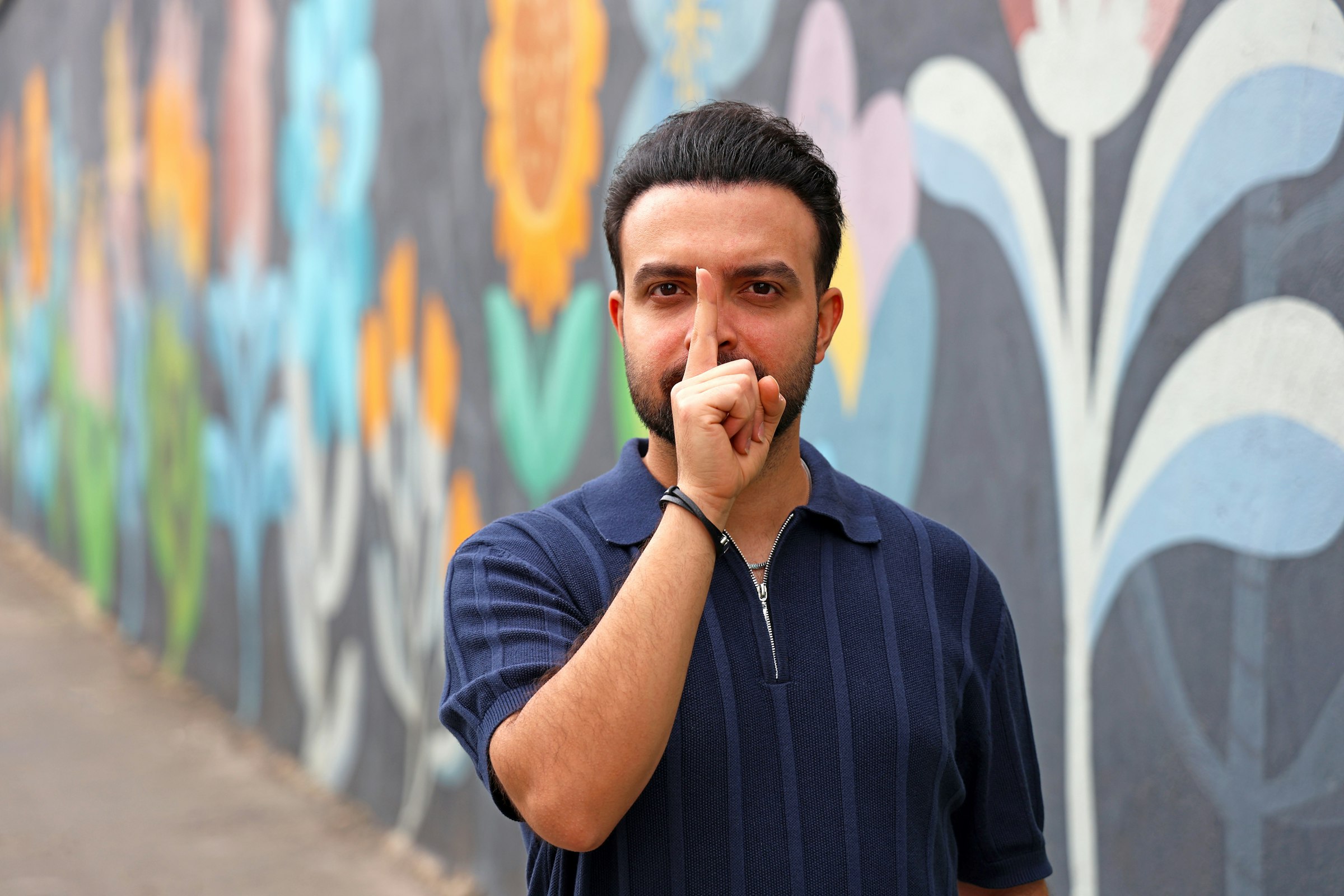 Man touches nose in front of colorful mural