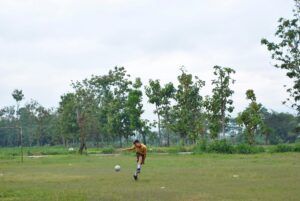 boy in brown shirt playing soccer on green grass field during daytime