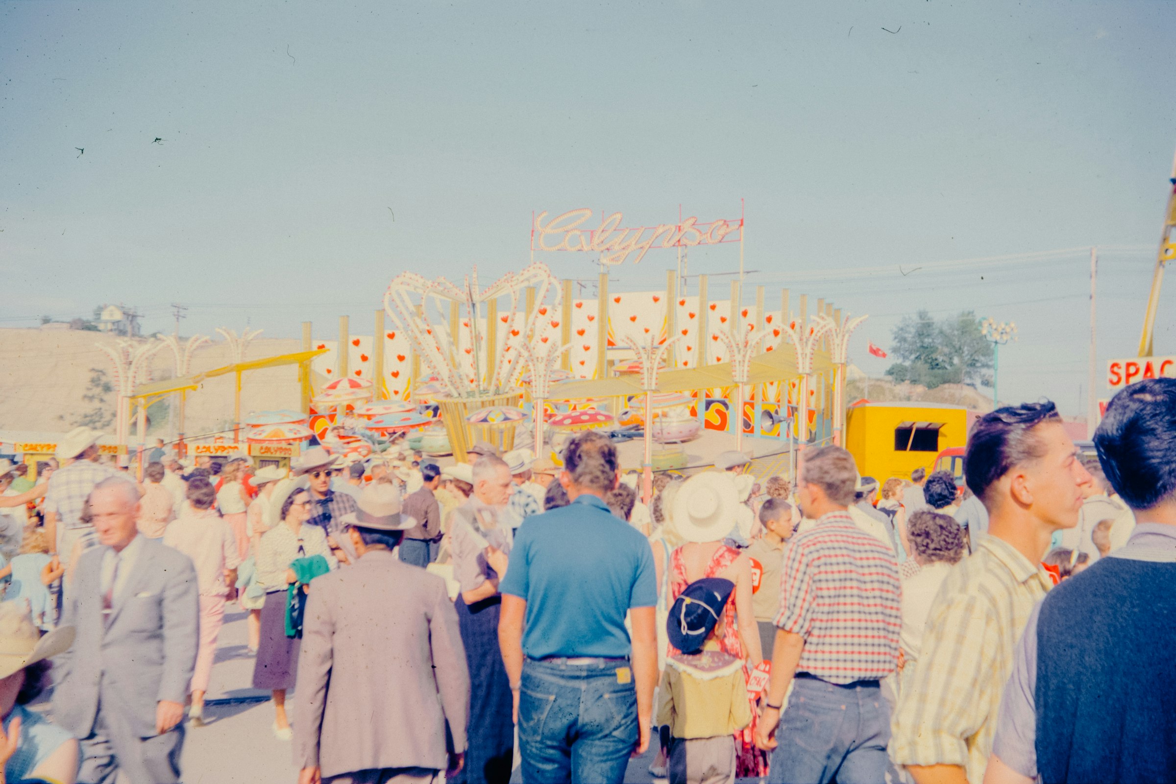 A crowd of people walking down a street next to a carnival ride