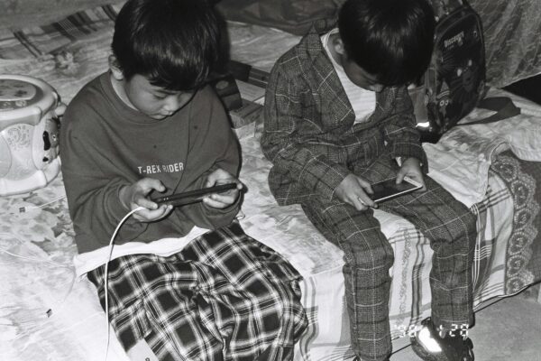 two young boys sitting on a bed looking at their cell phones