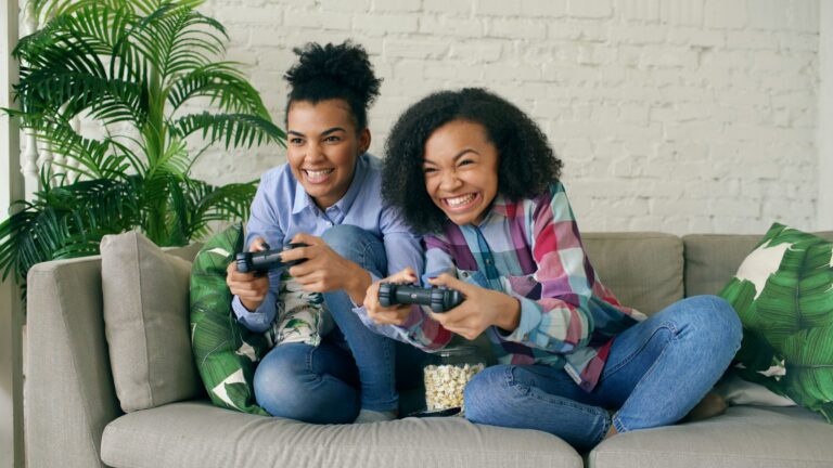 Two smiling women playing video games on couch